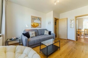 Another view of the living room, highlighting the gray sofa, a round coffee table, and warm wooden flooring.
