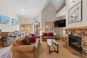 Living room with vaulted ceilings, gas fireplace, flatscreen TV, and access to private balcony.