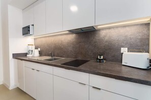 A modern kitchen with white cabinets, a sleek dark backsplash, and built-in appliances.
