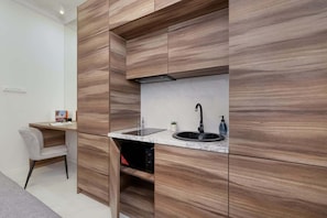 A compact kitchenette clad in wood-grain cabinetry, equipped with a sink and small workspace.
