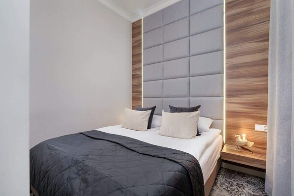 A stylish bedroom featuring a padded grey headboard, white pillows, and a dark throw.
