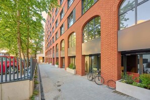 The exterior of a red-brick building with arched windows and a tree-lined walkway.
