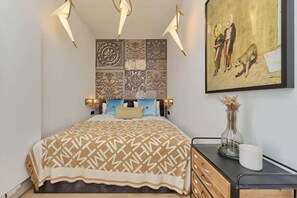 A stylish bedroom featuring a patterned bedspread, wall art, and decorative lighting.
