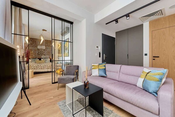 A modern living room with a light pink sofa, glass coffee table, and large windows.
