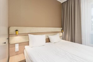 A bedroom with a double bed, soft bedding, and curtains, offering a serene and restful atmosphere.
