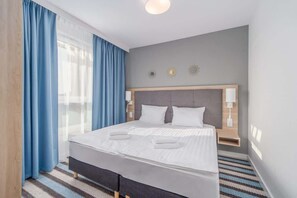 A cozy bedroom with a double bed, white bedding, and blue curtains, creating a calm and relaxing atmosphere.
