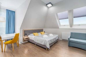 A cozy bedroom with a sloped ceiling, featuring a comfortable bed, a work desk, and skylight windows for natural light.
