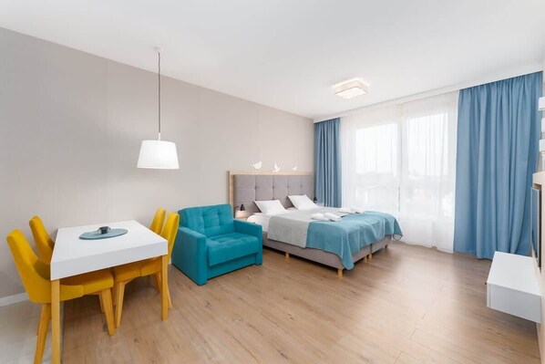 A modern open-plan living and dining area with a blue sofa, yellow chairs, and a clean, bright layout.
