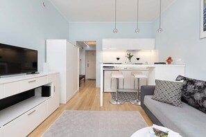 A wide-angle shot of the living area, showing the sofa, table, and kitchenette with minimalistic design.
