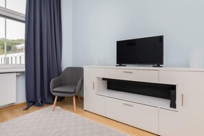 A flat-screen TV mounted above a sleek white console, next to a window with blue curtains.
