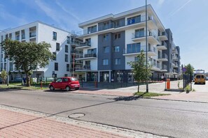 The exterior of a modern apartment building with a paved street and green landscaping.
