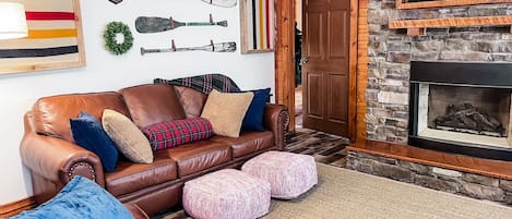 The living area at Whispering Pines features cozy leather seating, gas fireplace, Smart Tv, and windows that look out over the pine trees.