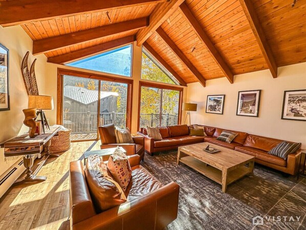 Step inside and be greeted by an expansive open-concept living area, featuring a cozy wood-burning fireplace and a large L-shaped leather sofa.