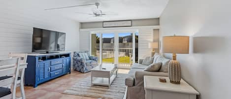 Living room with comfortable furnishings, a large smart TV, and sliding glass doors that lead to the ocean-view balcony