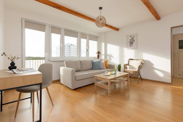 A spacious living room with wooden floors, a white sofa, and large windows letting in natural light.
