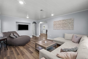 Living room with view into kitchen/dining area. TV and double chaise lounger.
