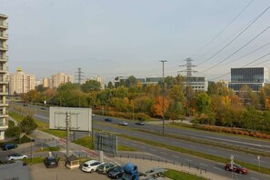 A view from the balcony overlooking a busy road, greenery, and city buildings in the distance.
