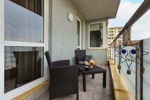 A balcony with a small seating area, overlooking the city and featuring a decorative wrought iron railing.
