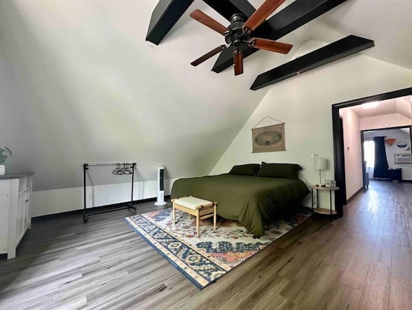 Vaulted ceiling w/ beams, King bed, sofa chair, floor length mirror, and cabinet