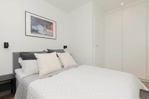 A cozy bedroom with a double bed, soft bedding, and a framed artwork on the wall.
