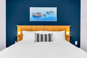 Step into the master king bedroom of our mid-century boho retreat, where warm reds and blues create a harmonious and inviting atmosphere. The centerpiece is the wooden bed, with crisp white linens, and golden lamps. The room has a personal desk and ROKU TV