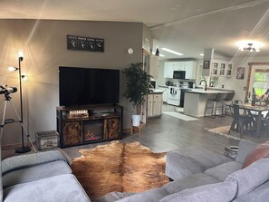 Open concept living with electric fireplace, large couch, & smart TV