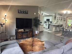 Open concept living with electric fireplace, large couch, & smart TV