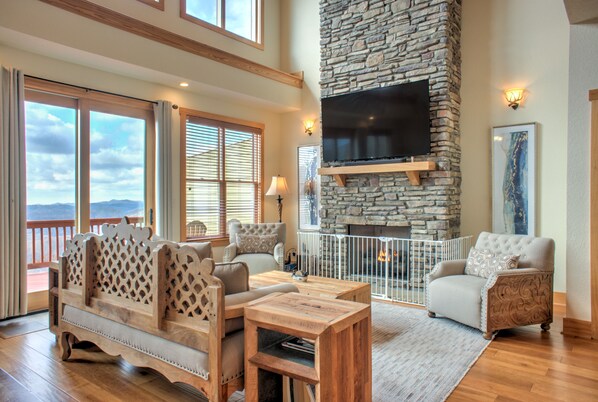 Relax in the beautifully furnished living room featuring a stone fireplace, large windows, and comfortable seating, making it the perfect retreat.