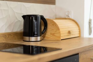 A kitchen corner with a wooden countertop, electric kettle, and a bread box, maintaining a clean and functional cooking area.
