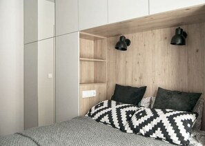 A cozy bedroom nook integrated into the living space, featuring a wooden frame and geometric-patterned pillows.
