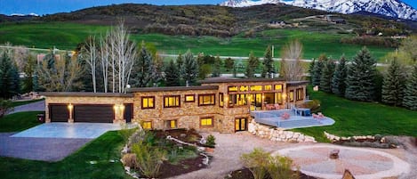 A view of the back of the home in the evening, showing the three car garage and expansive patio area, as well as the stunning mountain range.