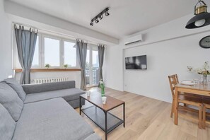 The living area seen from a different perspective, emphasizing the generous windows, gray curtains, and the dining space.

