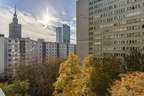 A city view from the window, featuring modern high-rise buildings and lush autumn trees.
