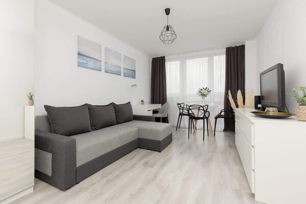 A bright living room with a gray sofa, a dining table, and modern decor in a minimalist white interior.

