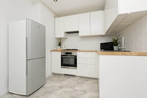 A modern kitchen with white cabinetry, a stainless steel refrigerator, and a wooden countertop.
