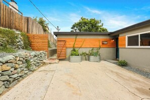 Modern mid-century style home with unique wood paneling, a spacious driveway, lush planter accents, and a rustic stone retaining wall, blending natural elements with contemporary architecture in a serene setting.