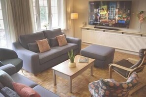 Living Room. It's a large area in which we've created different spaces - a space to relax and chat, a space to watch the 75'' TV, another for books/music. 
Having said all that, feel free to move the furniture and create the right space for you!