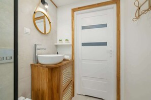 A compact bathroom corner featuring a wooden vanity, round mirror, and a sleek white door with glass panels.
