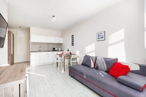 Another angle of the living area, featuring a gray sofa, a white dining table, and a minimalist kitchen.

