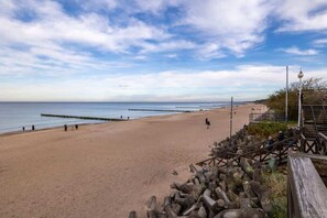 A sandy beach with a calm sea, wooden fences, and a clear blue sky.

