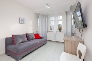 A modern living room with a gray and red sofa, a mounted TV, and a small dining area.

