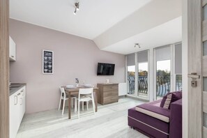 An open-plan living area with a purple sofa, dining table, and kitchen in a neutral color scheme.

