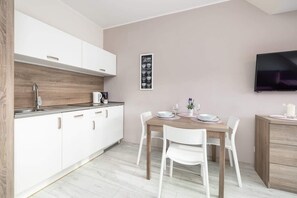 A compact kitchen with white cabinets, wooden accents, and a small dining area.

