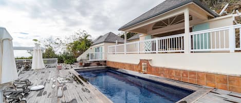 Grande terrasse en teck avec chaises longues entourant une belle piscine, face à la vue panoramique. 