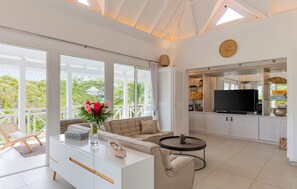 Situé au niveau principal, salon climatisé avec haut plafond, canapés blancs confortables avec coussins noirs et à motifs, table basse noire, télévision à écran plat haute définition avec Dish Network satellite, ainsi que les chaînes de télévision Orange 