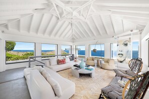 Située dans la villa principale. Magnifique salon climatisé avec superbes vues sur l'océan, accès au coin cinéma en sous-sol par un escalier. 
