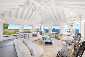 Située dans la villa principale. Magnifique salon climatisé avec superbes vues sur l'océan, accès au coin cinéma en sous-sol par un escalier.