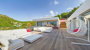 Sur la terrasse au niveau principal, grand salon extérieur moderne. Table à manger sous un ajoupa près de la piscine chauffée.