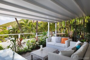 Lounge area with sofa on the covered terrace, facing the panoramic view over Gustavia. 