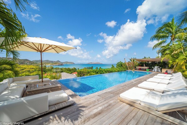 Large heated pool with expansive teak terrace, with deckchairs. Outdoor lounge area facing the view.